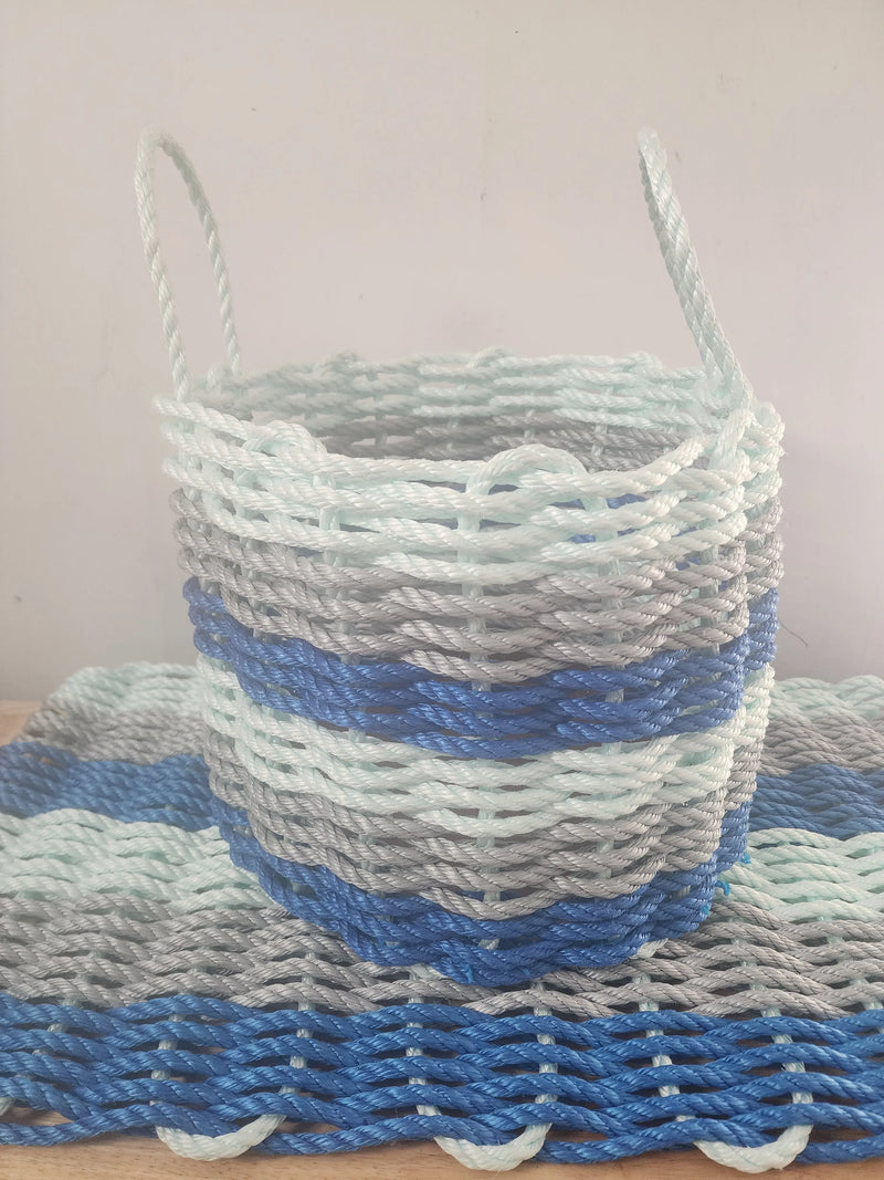 Image shows a Doormat and Basket, Matching set. 6 stripes in the color pattern, Blue, light gray, seafoam, blue, light gray, seafoam