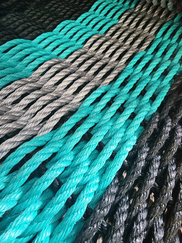 Photo shows a 5 Stripe Rope Welcome Mat. Colors are Black, Teal, Light Gray, Teal, Black. 